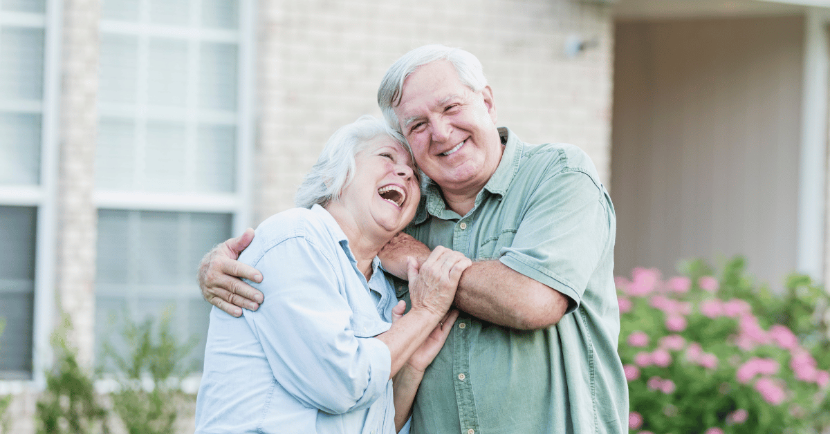 Couple senior souriant devant maison